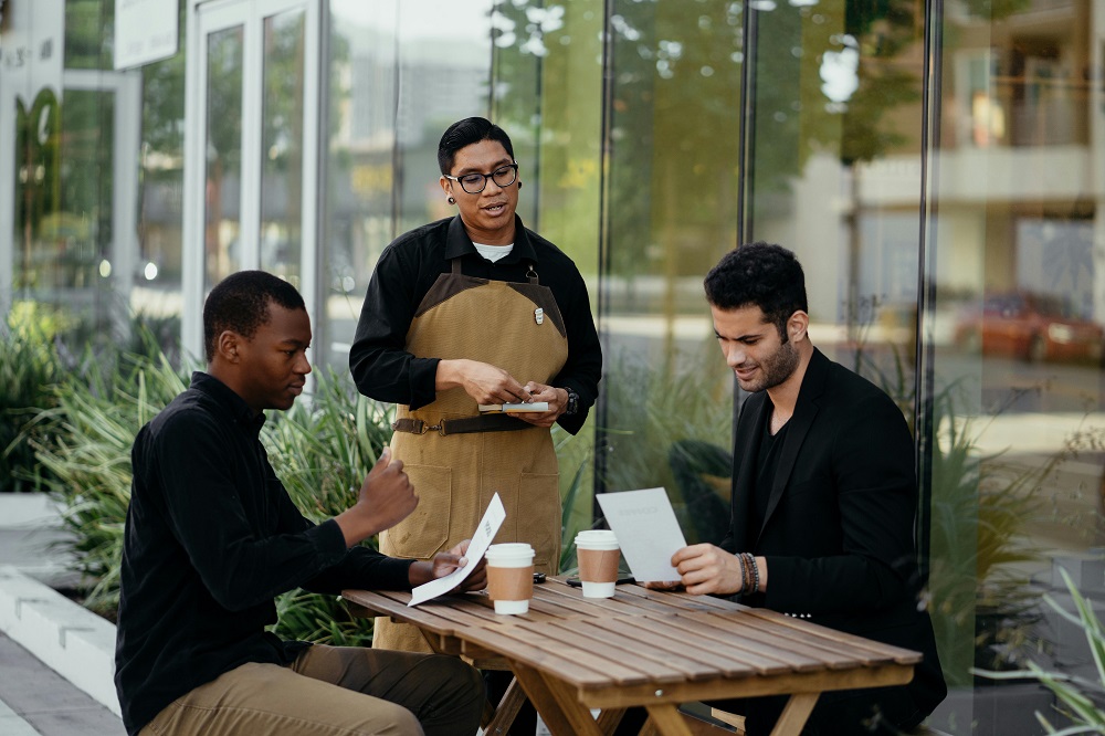 A waiter at the restaurant is helping customers with their orders.