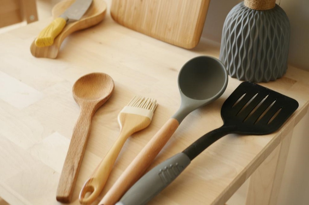 Black plastic cookware, silicone cookware and wood cookware on the kitchen stovetop.