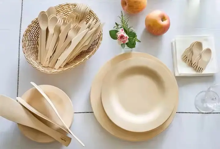 Biodegradable birch dinnerware on the table including disposable plates, disposable cutlery sets and wooden sporks.