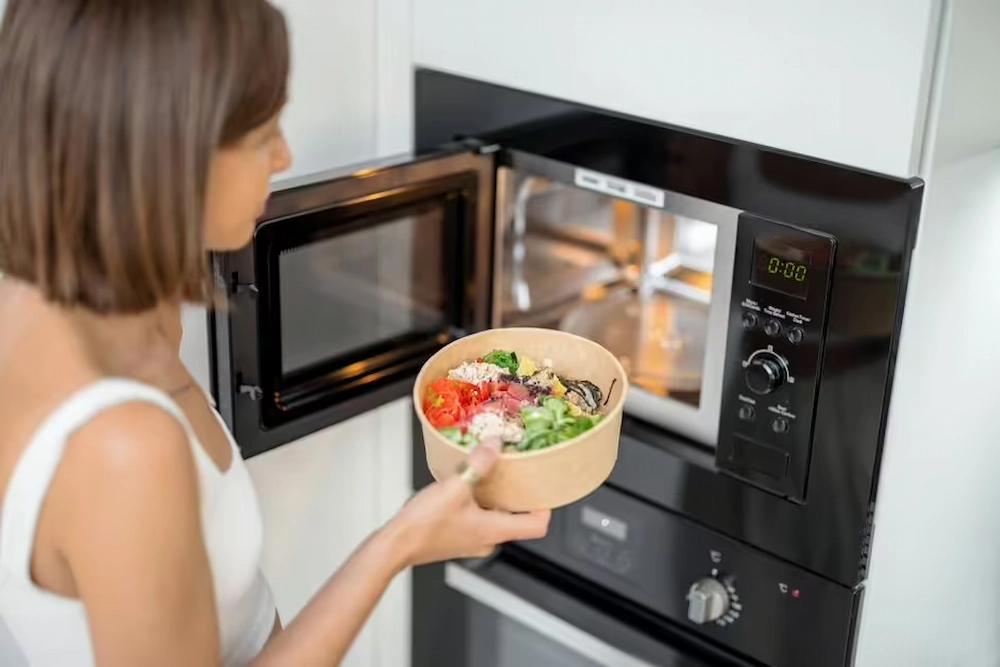 A woman is putting a paper bowl in microwave.