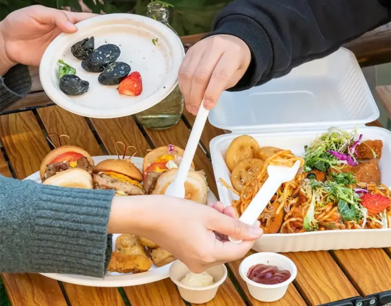 Customers enjoy their meals using sugarcane bagasse products, including disposable sugarcane bagasse plates, clamshell containers, forks, and sauce cups.